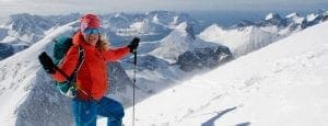 woman in orange jacket walking up mountain in winter